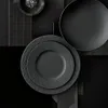 A collection of black plates and a small bowl with salt arranged on a dark, textured background. Anteprima dell’immagine prodotto