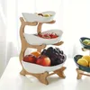 A three-tiered fruit stand made of bamboo with white ceramic bowls filled with various fruits. Náhled obrázku produktu