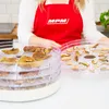 A person wearing a red apron is holding trays of dried mushrooms from a food dehydrator. Náhľad obrázku produktu