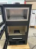A black wood-burning stove with its doors open, showing the interior with a rack and a grate. It is placed on a wooden pallet. Produktbild-Vorschau