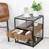 A modern side table with a glass top, wooden drawer, and metal frame, decorated with plants and a small deer figurine. Produktbild-Vorschau