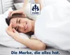 A woman is lying in bed, smiling and stretching. Produktbild-Vorschau