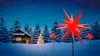 A snowy winter scene with a cabin, a decorated Christmas tree, and several red star-shaped garden stakes illuminated by warm white LEDs. Produktbild-Vorschau