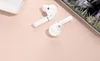 A pair of white wireless earbuds and their charging case are arranged on a light pink surface, with a smartphone screen visible in the background. Náhľad obrázku produktu