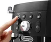A close-up shot of a person's finger pressing a button on a black DeLonghi espresso machine. Produktbild-Vorschau