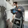 A man is using a rotary hammer to break apart a tiled wall while standing on a ladder. Produktbild-Vorschau