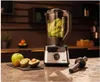 A blender with kiwi slices inside, placed on a kitchen counter with fruits and a tamper nearby. Produktbild-Vorschau