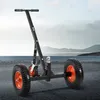 A black trailer mover with orange wheels is shown on a paved surface with a body of water and hills in the background. Produktbild-Vorschau