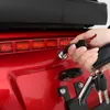 A hand is inserting a key into a lock on the back of a red vehicle. Produktbild-Vorschau