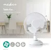 A white table fan is shown in front of a desk with a chair and some decorative plants. Podgląd zdjęcia produktu