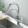 A modern chrome kitchen faucet with a pull-out spray and a separate filtered water spout, installed over a stainless steel sink. A wooden cutting board and stacked white bowls are visible on the left. Náhled obrázku produktu