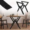 A dining table with black X-shaped legs, set in a room with chairs and decor. Produktbild-Vorschau