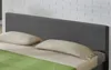 A close-up view of a bed with a gray fabric headboard, two beige pillows, and a green blanket. Produktbild-Vorschau