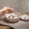 A hand is holding a bath bomb over a bowl of bath bombs, with a small decorative coral piece in a separate dish. Produktbild-Vorschau