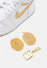A close-up view of a white Nike Air Jordan 1 Retro High sneaker with gold accents, accompanied by two gold shoelaces and a gold Nike Air Jordan charm. Podgląd zdjęcia produktu