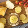 A close-up overhead view of cheese rounds, bread, and cherry tomatoes arranged on a wooden cutting board. Náhled obrázku produktu