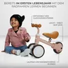 A young child sits on the floor next to a pink balance bike, with text overlays highlighting product features. Voir les images du produit