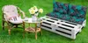 An outdoor seating area with a cat on a chair, a small table with flowers, and a pallet sofa. Produktbild-Vorschau