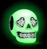A glowing green skull charm with diamond-like eyes and teeth, set against a dark background with green lighting. Produktbild-Vorschau