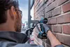 A person wearing safety gear is using a cordless impact wrench to attach a bracket to a brick wall. Voir les images du produit