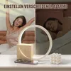A split image showing a woman waking up and stretching on the left, and sleeping on the right, with a sunrise alarm clock and phone charging in the foreground. Produktbild-Vorschau