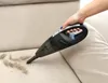 A hand is using a black handheld vacuum cleaner to clean debris from a light beige couch. Náhled obrázku produktu