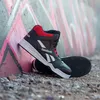 A pair of black and red high-top Reebok sneakers leaning against a graffiti-covered wall. Náhľad obrázku produktu