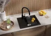 A modern kitchen sink area with a black granite sink, faucet, lemons, and a pitcher of green liquid. Produktbild-Vorschau
