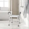 A shower chair is placed in a bathroom next to a bathtub, with a showerhead and towel visible. Podgląd zdjęcia produktu