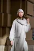 A woman wearing a knitted outfit stands in front of a textured wall. Produktbild-Vorschau