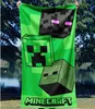A person is holding up a Minecraft-themed towel outdoors, with trees and water in the background. Produktbild-Vorschau