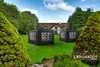 Two black party tents are set up on a green lawn in front of a thatched-roof house. Produktbild-Vorschau