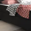 A close-up view of a black box spring bed with patterned pillows and blankets. Produktbild-Vorschau