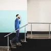 A man is walking up stairs while talking on his phone, holding onto a metal handrail. Náhľad obrázku produktu