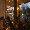 A string of star-shaped lights hanging in a window at dusk, with a pine branch in the foreground. Produktbild-Vorschau