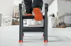 A person's feet are shown stepping onto a black and red step stool in a room with construction materials. Náhľad obrázku produktu