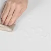 A hand is wiping a white surface with a cloth, and there are water droplets on the surface. Produktbild-Vorschau