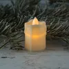 A close-up of a battery-operated LED candle with a flickering flame, placed on a rustic wooden surface with a frosted pine branch in the background. Produktbild-Vorschau