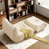 A beige sofa and ottoman are placed on a rug in a room with bookshelves and a window. Náhled obrázku produktu