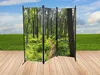 A folding screen with a forest motif is placed on a wooden deck in front of a grassy field and a blue sky with clouds. Produktbild-Vorschau