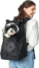 A woman is wearing a black dog carrier backpack with a small dog inside. Produktbild-Vorschau