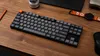 A keyboard and other desk accessories are arranged on a wooden desk. Produktbild-Vorschau