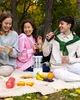 Three young adults are having a picnic in a park, with a juicer and fruits on a blanket. Produktbild-Vorschau