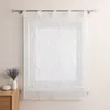 A sheer white curtain with green wavy embroidery and small green beads is hung on a curtain rod in front of a window. A small vase with lavender and a white decorative object are on a wooden dresser to the left of the curtain. Produktbild-Vorschau