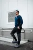 A man stands on steps next to a building, wearing sweatpants and a hoodie. Podgląd zdjęcia produktu