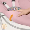 A close-up of a pink baby bouncer with a hand pressing on the fabric, and a washing machine icon in the lower left corner. Produktbild-Vorschau