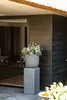 A plant pot on a pedestal in front of a dark wooden wall. Produktbild-Vorschau