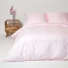 A close-up view of a pink striped duvet cover and pillowcase on a bed, with a wooden nightstand and a vase of flowers in the background. Náhled obrázku produktu