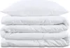 A stack of white bedding, including a pillow and two folded duvets, is presented against a white background.
