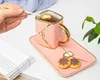 A hand is holding a spoon over a pink teacup and saucer set with cookies. Produktbild-Vorschau